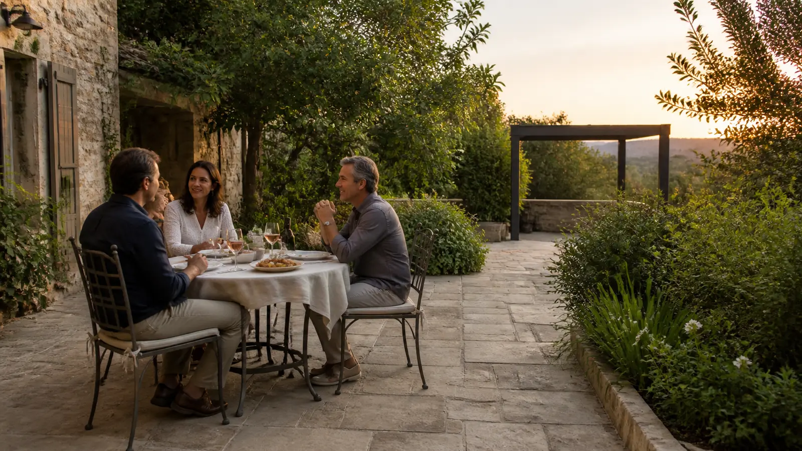 Trois personnes prennent un repas sur une terrasse laissant un passage libre vers le jardin