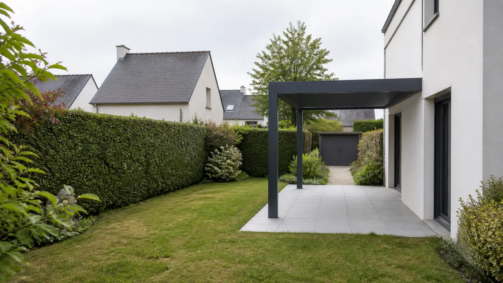 Pergola anthracite en bord de terrasse avec haie haute, jardin et maisons voisines en arrière-plan
