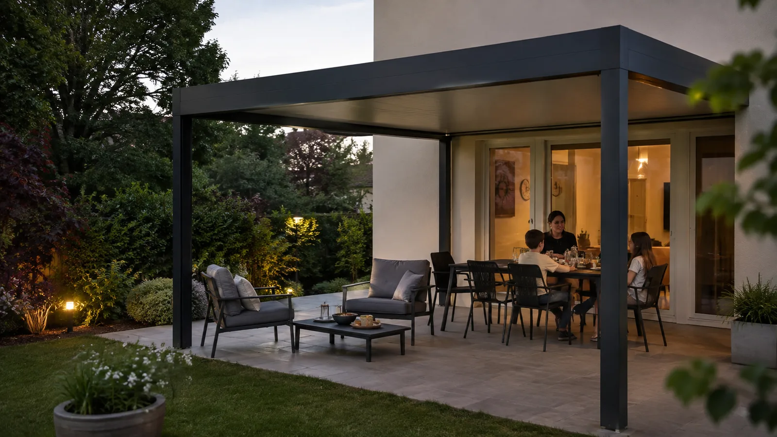 Salon bas et table de repas sous une pergola adossée au crépuscule dans un jardin