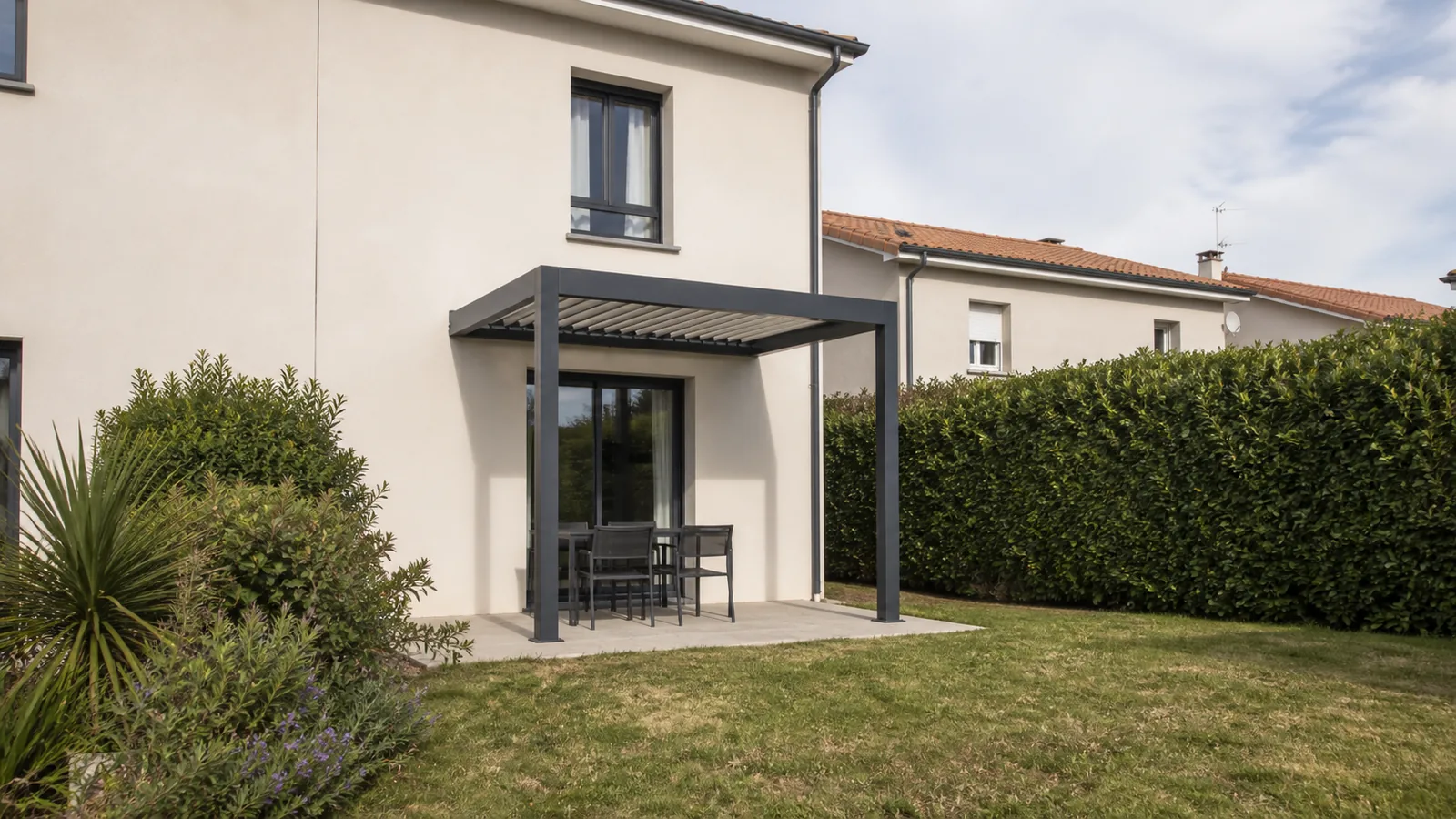 Petite pergola anthracite adossée à une maison vue depuis le jardin avec haie et logements voisins