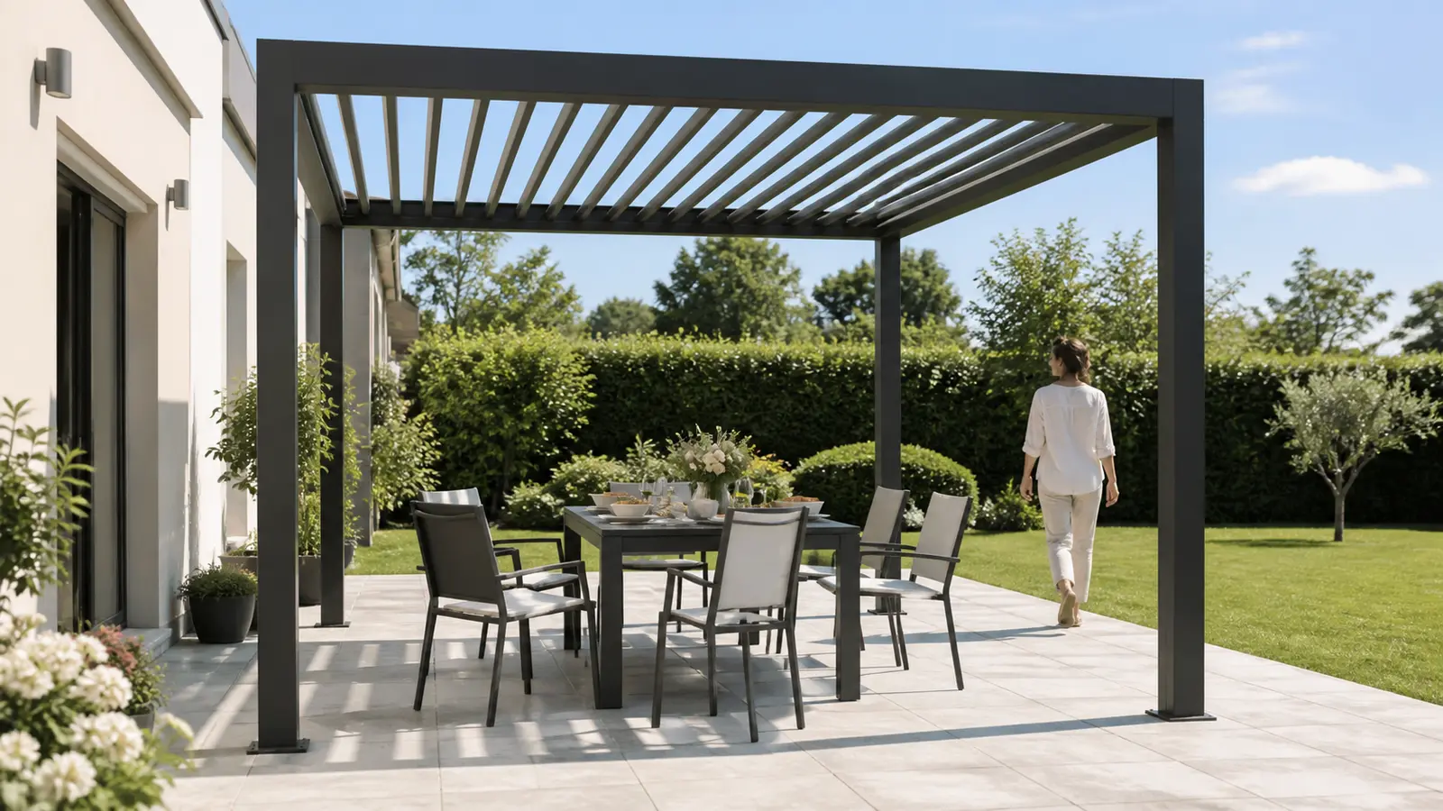 Table dressée sous une pergola carrée avec chaises reculées et personne circulant vers le jardin