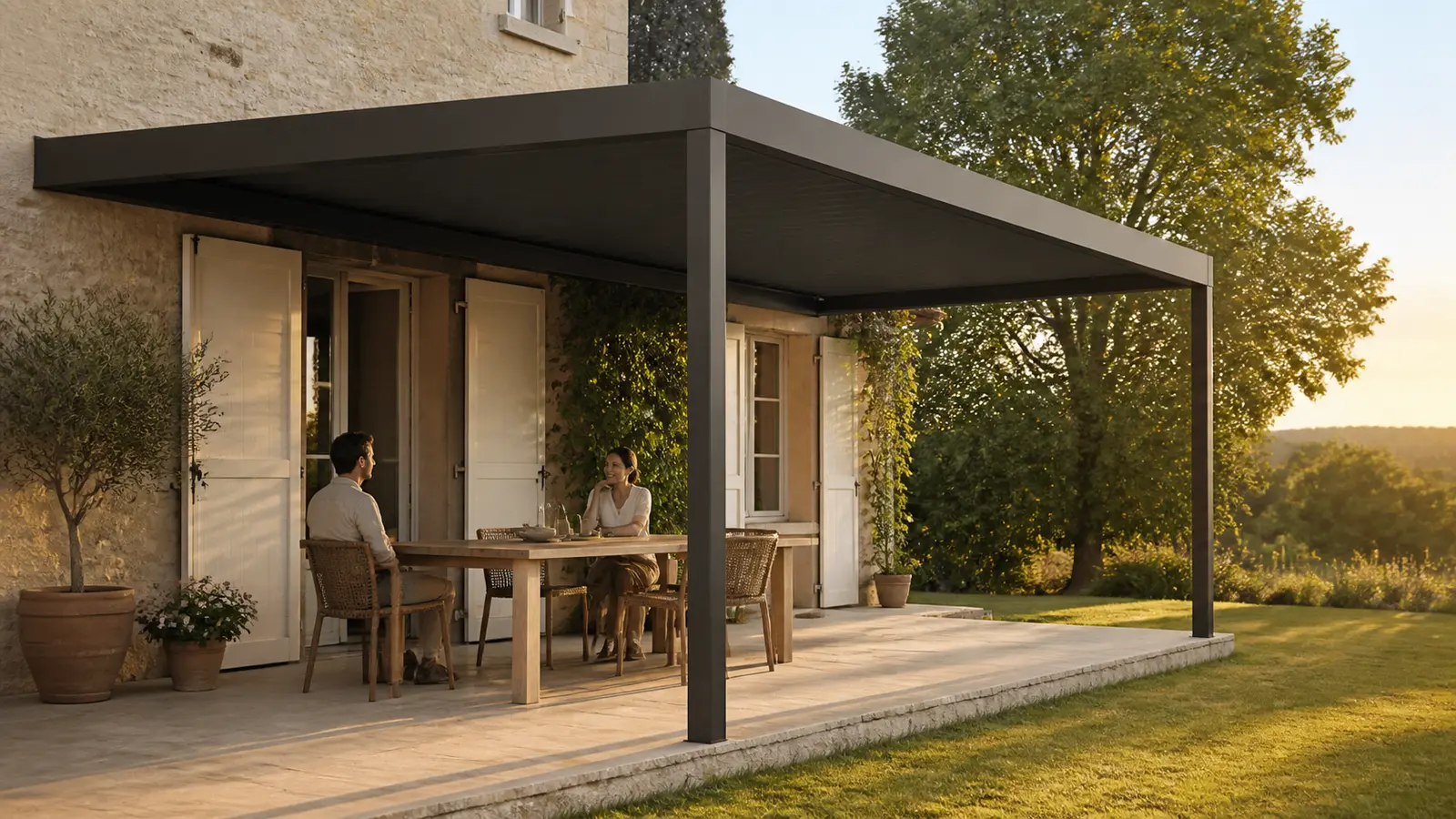 Couple attablé à l’ombre sous une pergola anthracite face à un jardin éclairé en fin de journée