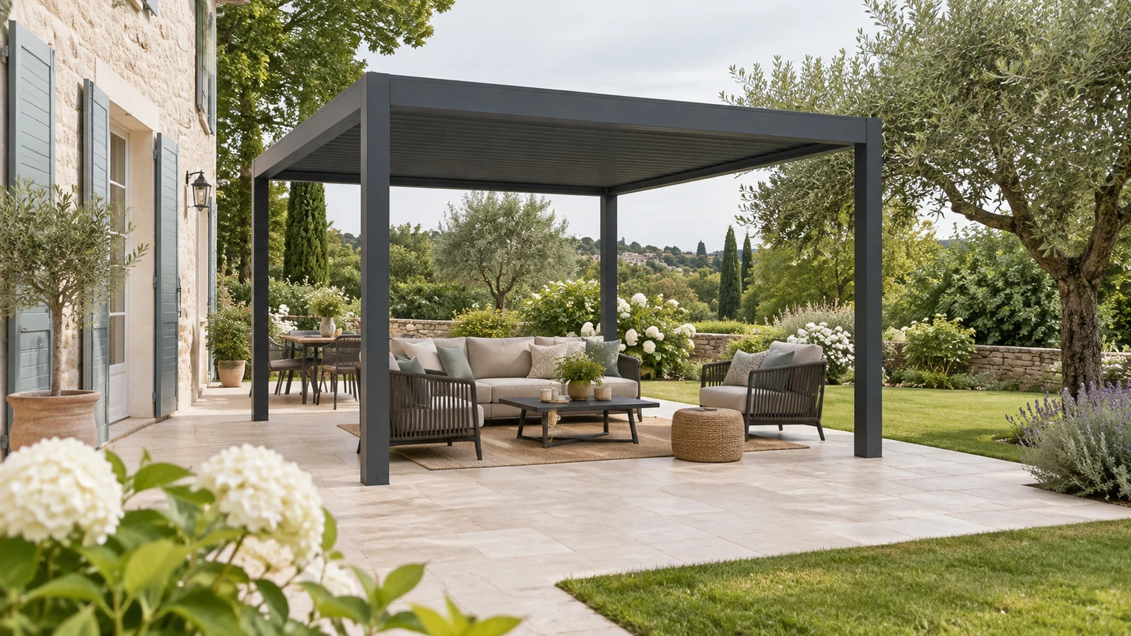 Pergola autoportée anthracite sur une terrasse dallée avec salon extérieur et transition vers le gazon