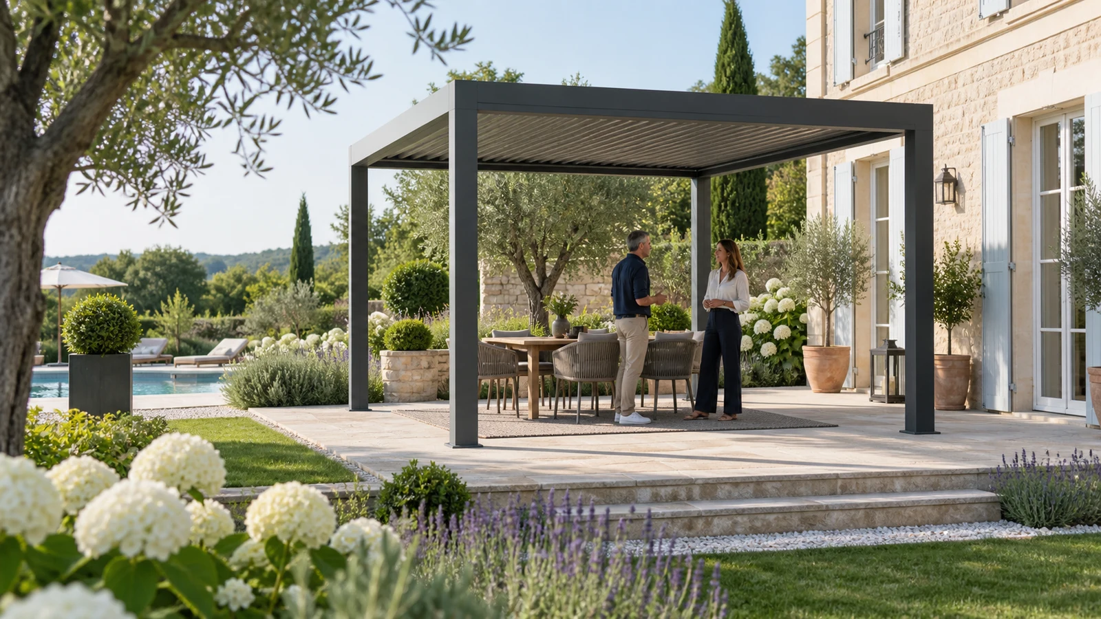 Deux adultes discutant sous une pergola autoportée anthracite dans un jardin avec piscine en arrière-plan