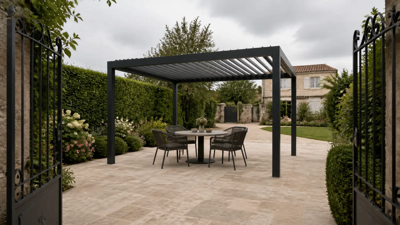 Pergola autoportée anthracite avec table ronde dans une cour pavée accessible depuis un portail